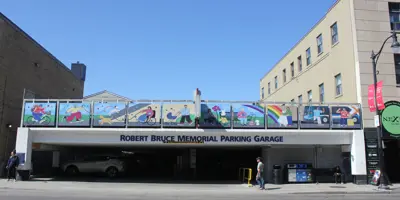 Image shows a parking garage entrance on a street with 10 art panels above the entrance showing bright illustrated figures engaging in activities such as walking, riding a bike, and boarding a bus.