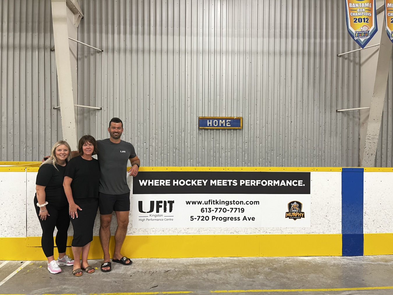 L-R Jules Fournier, Sara Maveety, Josh Maveety from UFIT standing beside a new sign at the UFIT Rink at Centre 70 Arena.