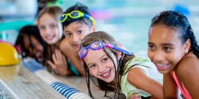 Five kids swimming and leaning on the edge of a pool.
