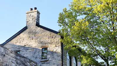 An image showing the top floor of an older limestone building next to a tree