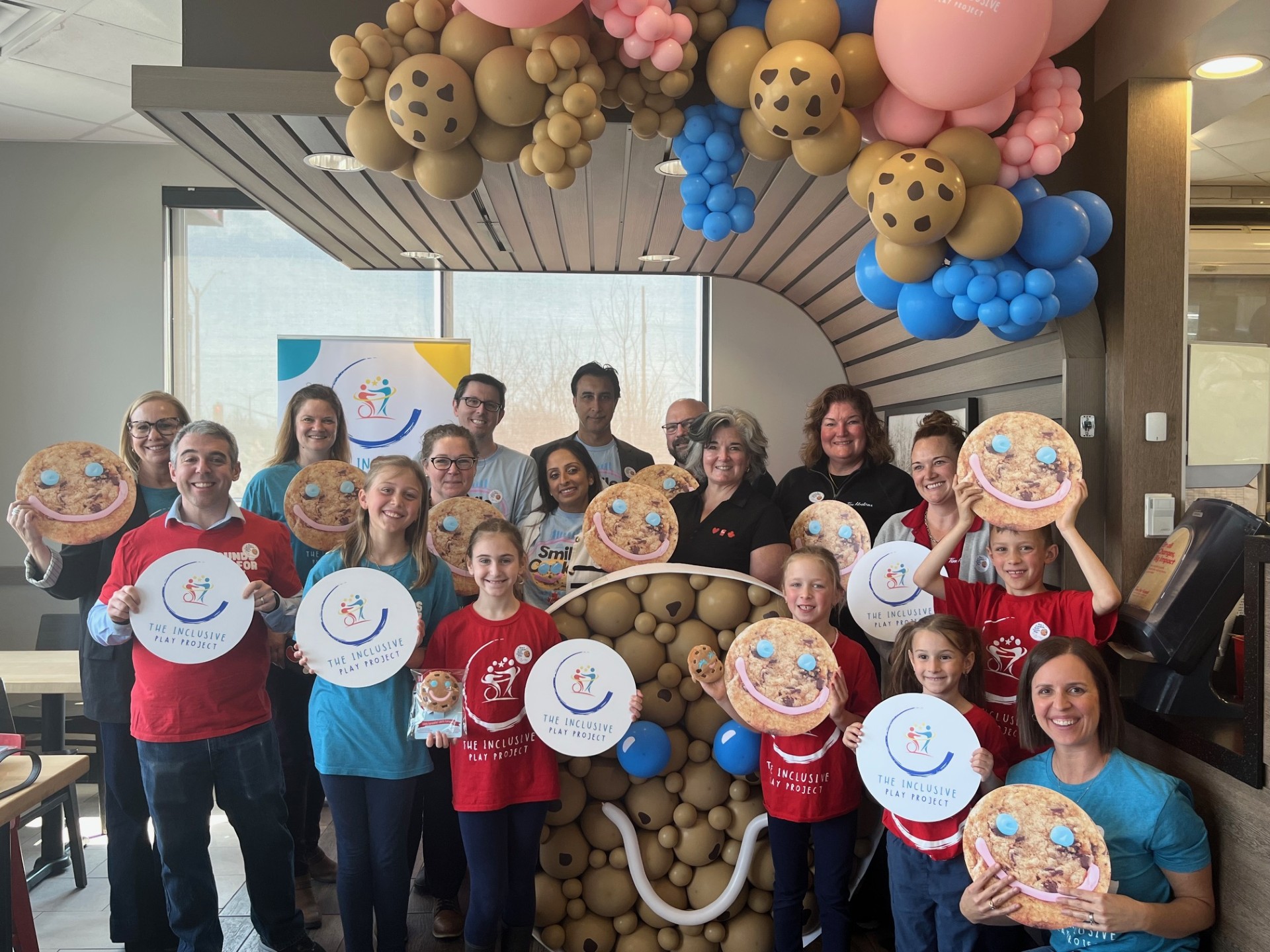 Volunteers of the Inclusive Play Project holding round signs with the inclusive play project logo and signs with a photo of a smile cookie.