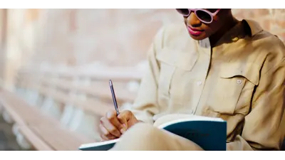 A woman sitting on a bench writing in a book