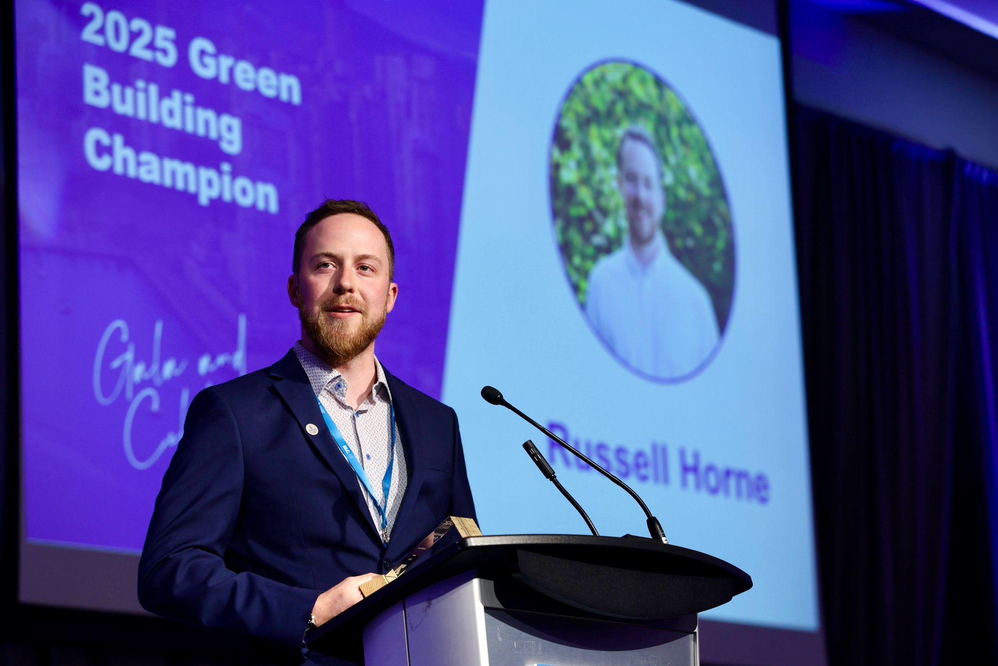 Russell Horne stands at a podium with a screen reading 2025 Green Building Champion in the background. Caption: Russell Horne, Manager of Facilities Energy & Asset Management, earned the Green Building Champion award.