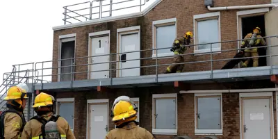 The fire training facility being used by two firefighters on the second floor outside, while three firefighters watch