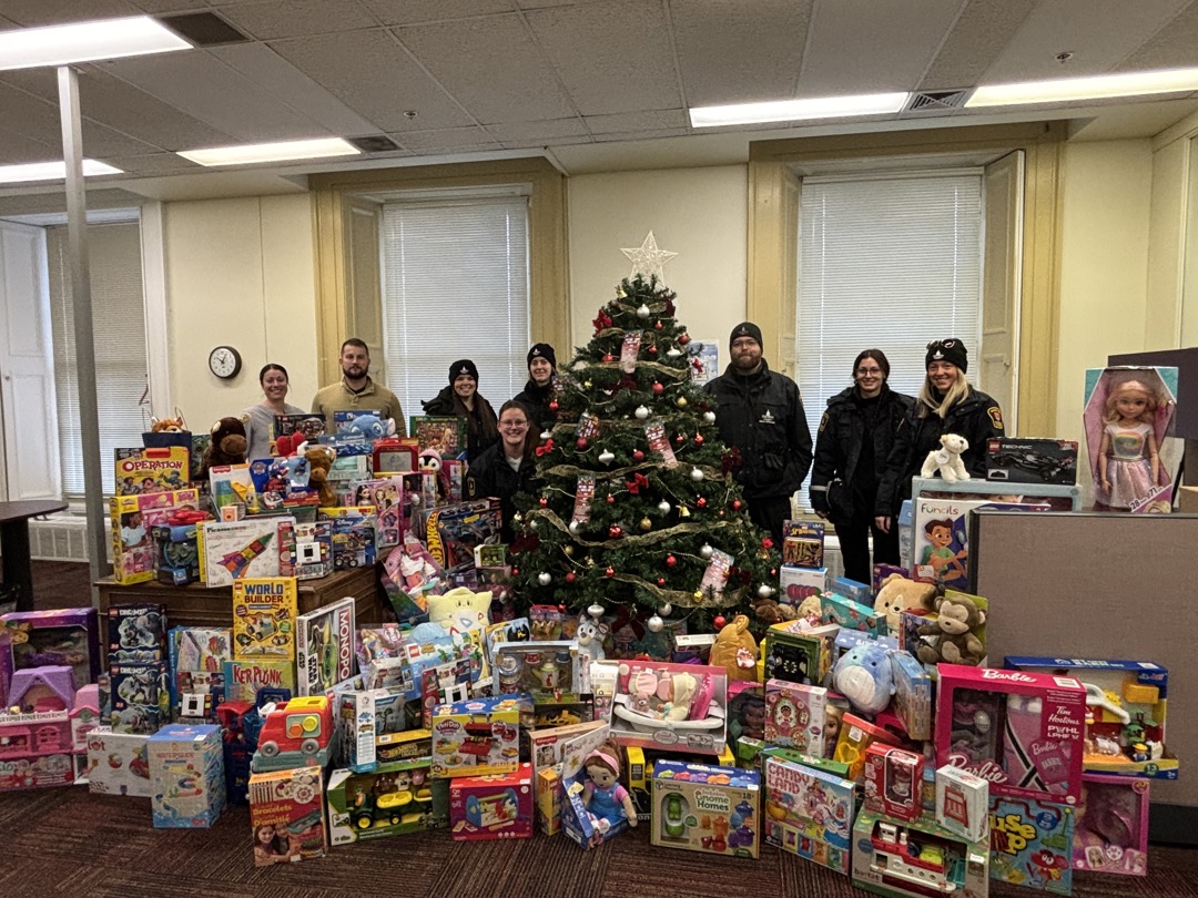 City Bylaw Enforcement staff stand around a Christmas Tree behind a large display of toys that were donated as part of the Toys for Tickets campaign.